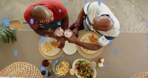 Overhead view of father and son clinking milkshakes at kitchen island sharing burgers