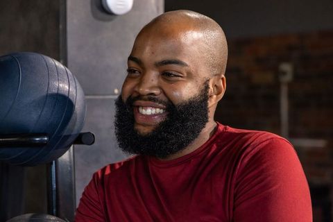 Smiling african american man wearing red long-sleeve shirt standing by gym medicine balls