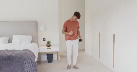 Young man celebrating with smartphone while standing in minimalist modern bedroom interior