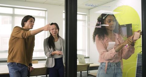 Diverse coworkers brainstorm ideas on glass wall
