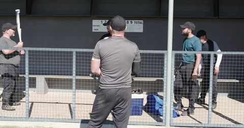 Baseball team gathering in dugout behind fence preparing for game strategy discussion