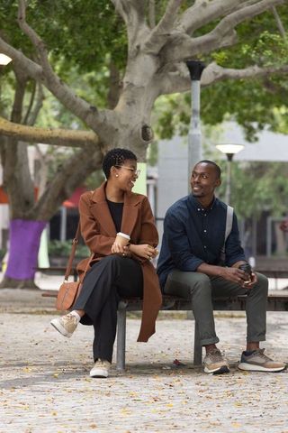 African american couple sitting and chatting on bench in urban plaza during autumn