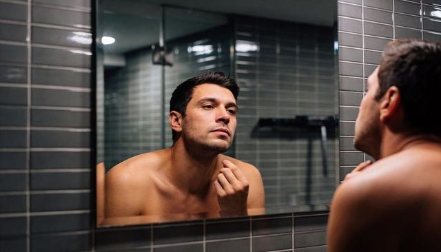 Barechested man inspecting chin in modern bathroom mirror grooming and skin care routine