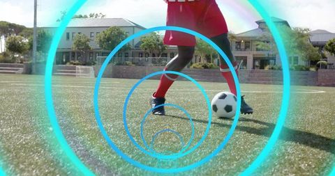 Male soccer player dribbling on school turf wearing red kit controlling ball with concentric cyan ri