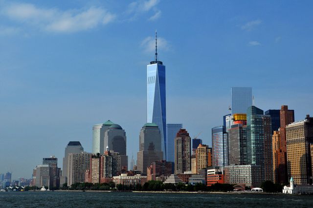 Dramatic view of Manhattan's iconic skyscrapers with Hudson River in foreground, featuring prominent buildings like One World Trade Center. Ideal for use in travel brochures, city guides, business promotions, and architectural magazines.