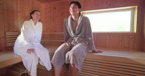 Diverse couple relaxing and chatting in wooden sauna wearing plush robes