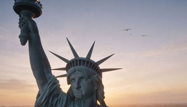 Statue of liberty close-up at sunrise showing torch crown spikes harbor silhouette