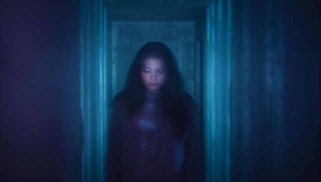 Moody blue-lit portrait of Asian woman standing in narrow hallway, introspective glow