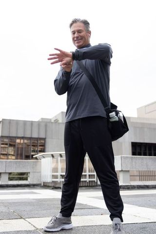 Mature man checking smartwatch before urban workout, carrying gym bag with water bottle