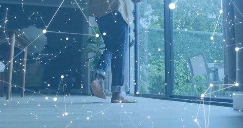 Barefoot man stepping through glass doors in modern home with digital network overlay