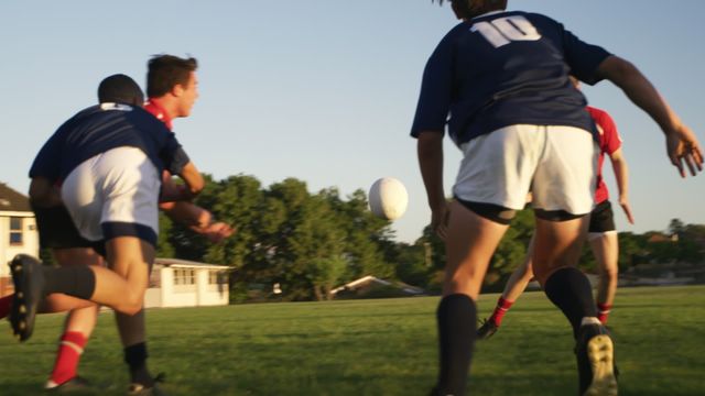 Young athletes competing in youth rugby match under bright blue sky on grassy field, demonstrating teamwork and athletic skills. Perfect for use in sports promotional materials, articles on youth sports activities, or inspirational content focused on teamwork and athleticism.