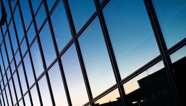 Dusk Glass Curtain Wall Reflecting Sky and Rooftop with Geometric Grid