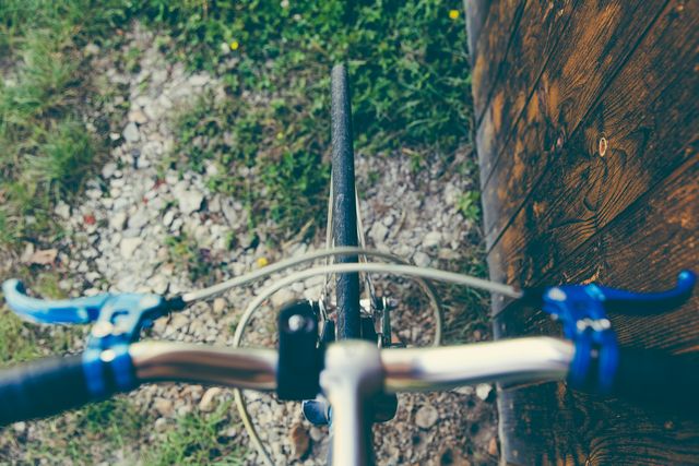 Close up view of a bicycle handlebar and front wheel on a gravel path, shot from above. Ideal for promoting outdoor activities, cycling tourism, fitness events, and travel websites. Can also be used in articles about healthy living, environmental transportation, and leisure activities.