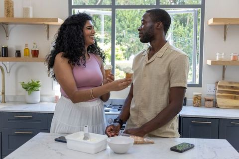 Smiling diverse couple sharing ice cream cones at bright kitchen island romantic moment