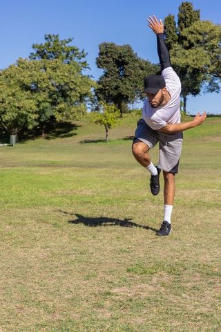 Athlete balancing mid-leap in park practicing agility, stretching and athletic training