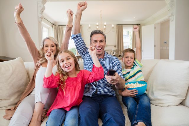 Family sitting on couch in living room, cheering and celebrating while watching a soccer match on television. Perfect for themes related to family bonding, sports enthusiasm, home entertainment, and leisure activities.