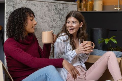 Friends enjoying coffee break amid moving chaos in kitchen