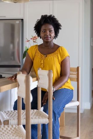 African american woman sitting at kitchen island wearing mustard blouse, cozy interior portrait