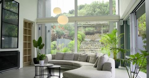 Light-gray curved sectional sofa facing floor-to-ceiling glass with lush garden view, modern minimal