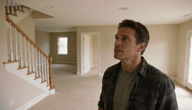 Man inspecting vacant sunlit living room with staircase during home inspection