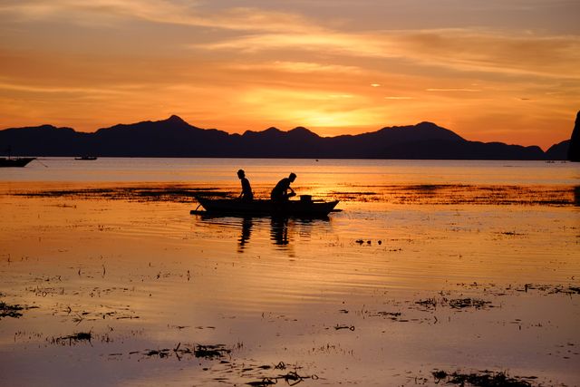This scenic image showcases two fishermen silhouetted against a vibrant sunset on a tranquil lake. Ideal for themes related to nature, serenity, outdoor activities, and peaceful moments. Perfect for use in travel blogs, landscape photography websites, brochures about fishing destinations, or calming and relaxing content.