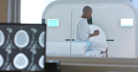 African woman sitting on ct scanner table wearing medical gown waiting diagnostic scan