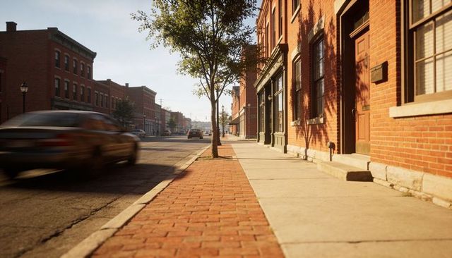 Sunlit small-town main street with red brick storefronts, tree-lined sidewalk and moving car