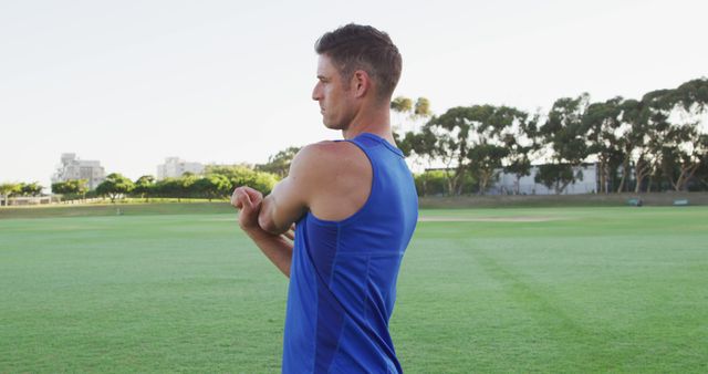 Smiling fit caucasian man exercising outdoors stretching from the waist. cross training for fitness at a sports field.