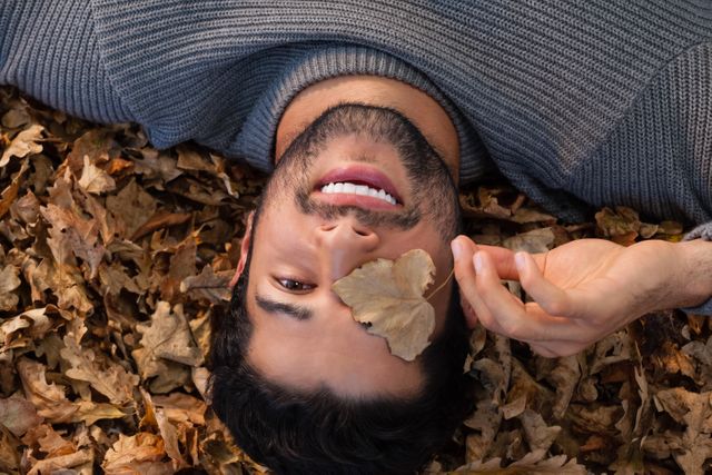 Man Lying on Autumn Leaves Holding Leaf Over Eye - Download Free Stock Photos Pikwizard.com