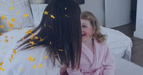 Caregiver leaning and playing with child laughing on bed in cozy robes with gold stars