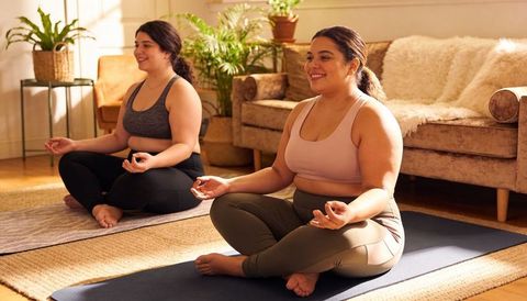 Plus-size women meditating together in sunlit cozy living room with plants