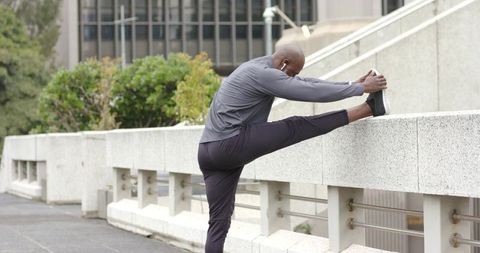 African american runner stretching on concrete railing in urban morning with earbuds