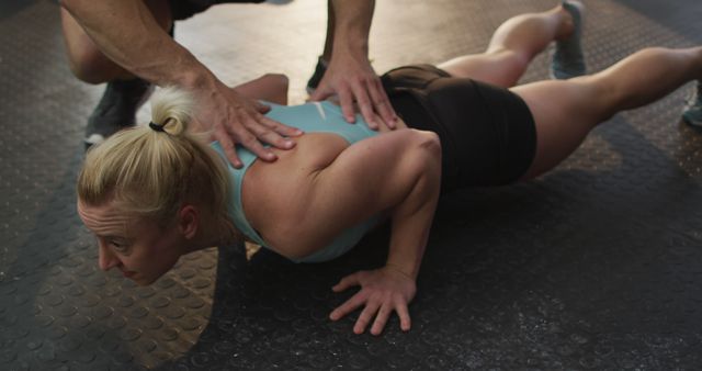 Woman doing push-up while being guided by a personal trainer. Ideal for illustrating personal training, gym sessions, fitness motivation, physical exercise routines, and coaching assistance in athletic training.