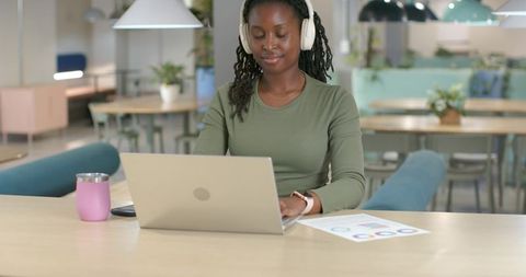 African American woman working on laptop at coworking space reviewing colorful charts