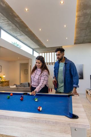 Couple playing pool at home on blue felt table casual game night in modern living room