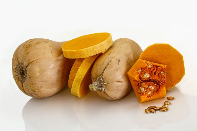 Depicts fresh butternut squash along with slices and seeds placed on a clean white background. Can be used in nutrition campaigns, autumn recipe blogs, cookbook illustrations, or health food advertisements.