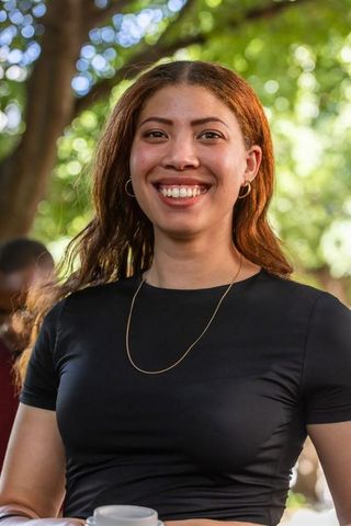 Sunlit african american woman smiling in park wearing black top and holding coffee mug