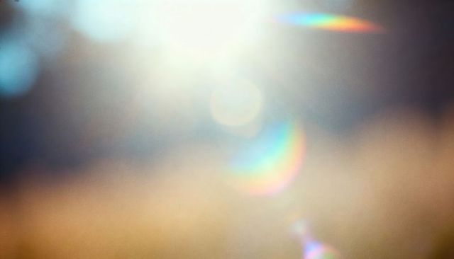 Overexposed sunlight creating rainbow lens flare and soft bokeh in hazy field
