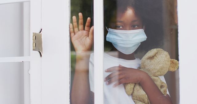 Young Girl in Face Mask Holding Teddy Bear and Waving Through Window - Download Free Stock Images Pikwizard.com