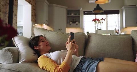 Relaxed Asian Woman Using Smartphone on Cozy Living Room Sofa