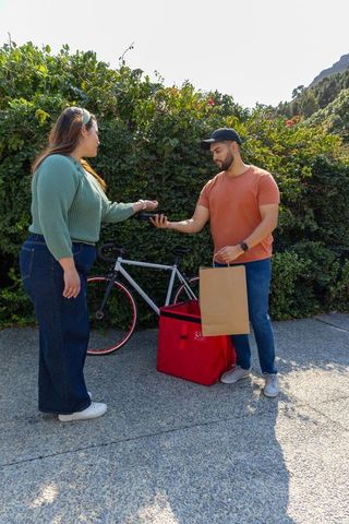 Bicycle courier delivering takeout to customer on sunny walkway with contactless payment