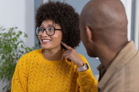 Smiling woman in yellow sweater showing smartwatch while chatting with partner at home