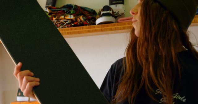 Teen girl holding skateboard in street style clothing store, wearing a beanie and casual clothing. Ideal for urban fashion advertisements, youth culture campaigns, skateboarding promotions, shopping themes, and retail marketing.