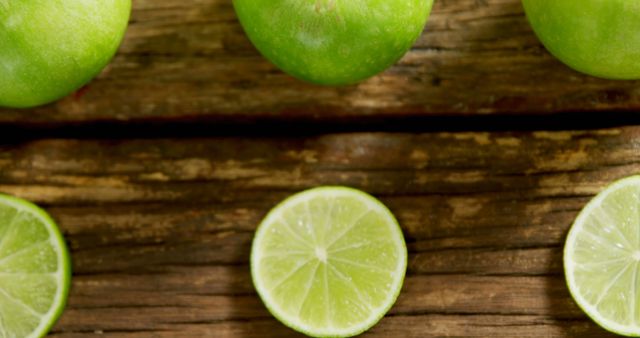 Close-up of fresh limes and lime slices arranged on a rustic wooden table. The image highlights the vibrant green color and texture of the limes, suitable for use in food blogs, recipe books, culinary websites, or advertisements for natural and healthy products.