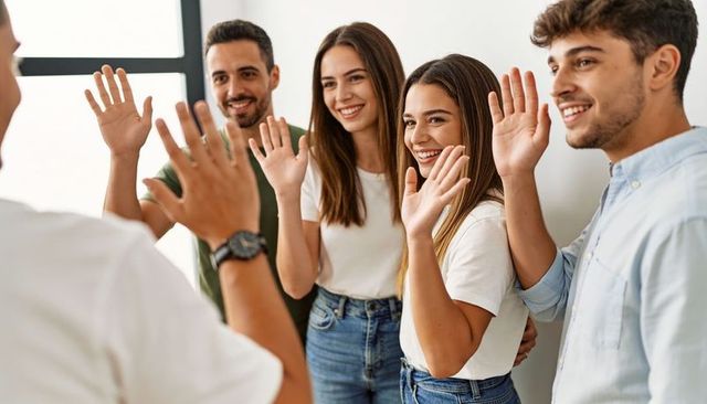 Young professionals raising hands and giving high five while smiling and greeting team