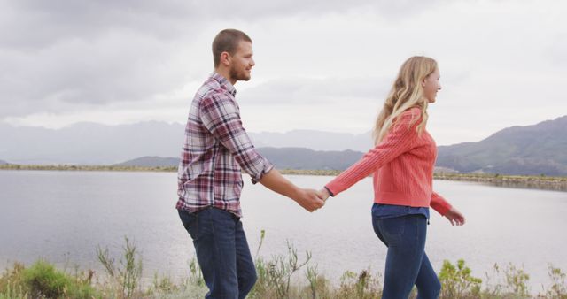 Caucasian couple walking by lake holding hands with copy space. Nature, travel, tranquility, lifestyle concept, unaltered.