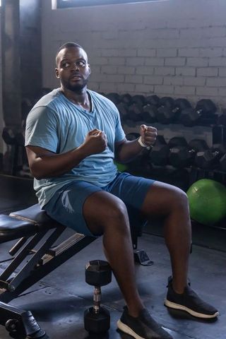 African man sitting on gym bench clenching fists showing strength focus and determination
