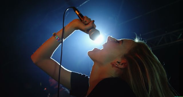 A young Caucasian female singer passionately performs on stage, with copy space. Her dynamic expression and the concert lighting create an energetic atmosphere.