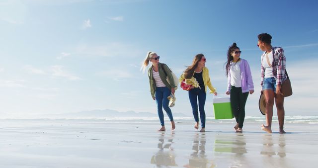 Group of friends enjoying time together on a sunny beach, walking and carrying a cooler. Perfect for travel agencies, youth lifestyle campaigns, summer vacation promotions, and outdoor leisure advertisements.