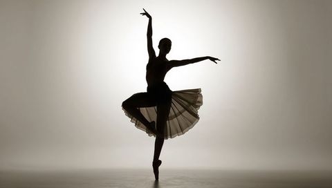 Ballerina silhouette en pointe in flowing tutu with halo backlight, dramatic studio